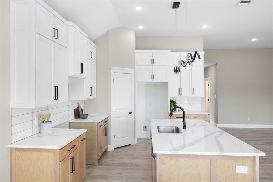 Kitchen with an island with sink, white cabinets, sink, and backsplash