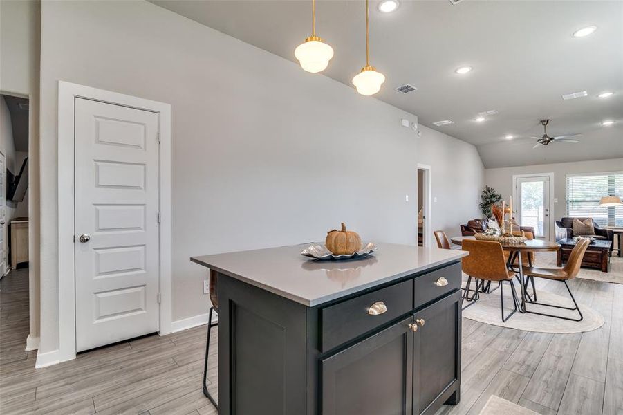 Kitchen with ceiling fan, pendant lighting, lofted ceiling, a center island, and light wood-type flooring