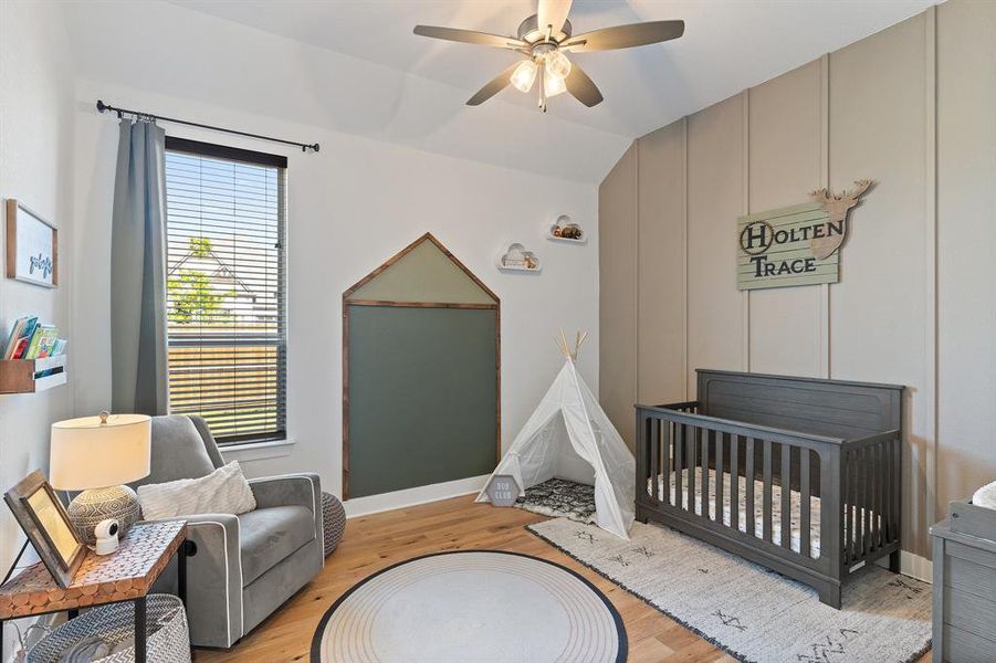 Bedroom with a nursery area, ceiling fan, and light wood-type flooring