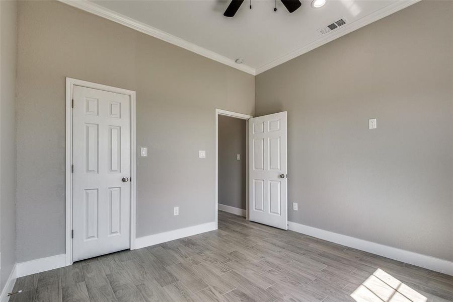 bedroom with a towering ceiling, light hardwood / wood-style floors, crown molding, and ceiling fan