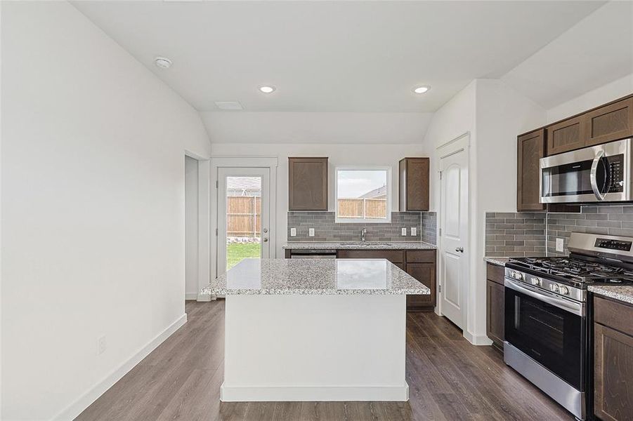 Kitchen featuring stainless steel appliances, wood-type flooring, vaulted ceiling, and a kitchen island