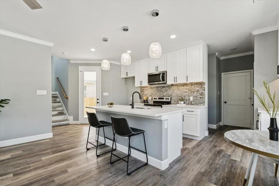 Kitchen featuring wood-type flooring, decorative light fixtures, a kitchen island with sink, white cabinetry, and stainless steel appliances