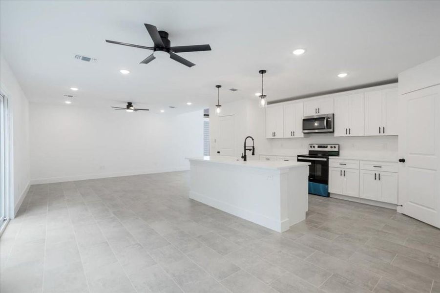 Kitchen with pendant lighting, a kitchen island with sink, stainless steel appliances, white cabinetry, and ceiling fan