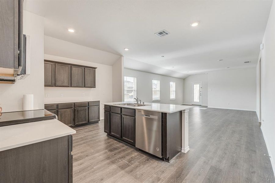 Kitchen with an island with sink, dark brown cabinets, light hardwood / wood-style flooring, stainless steel dishwasher, and sink