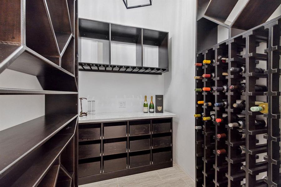 This wine room is the ultimate haven for wine aficionados, featuring temperature-controlled settings, sleek tile flooring, custom built ins, contemporary iron and brass pendant light, elegant quartz countertops and integrated wine storage.