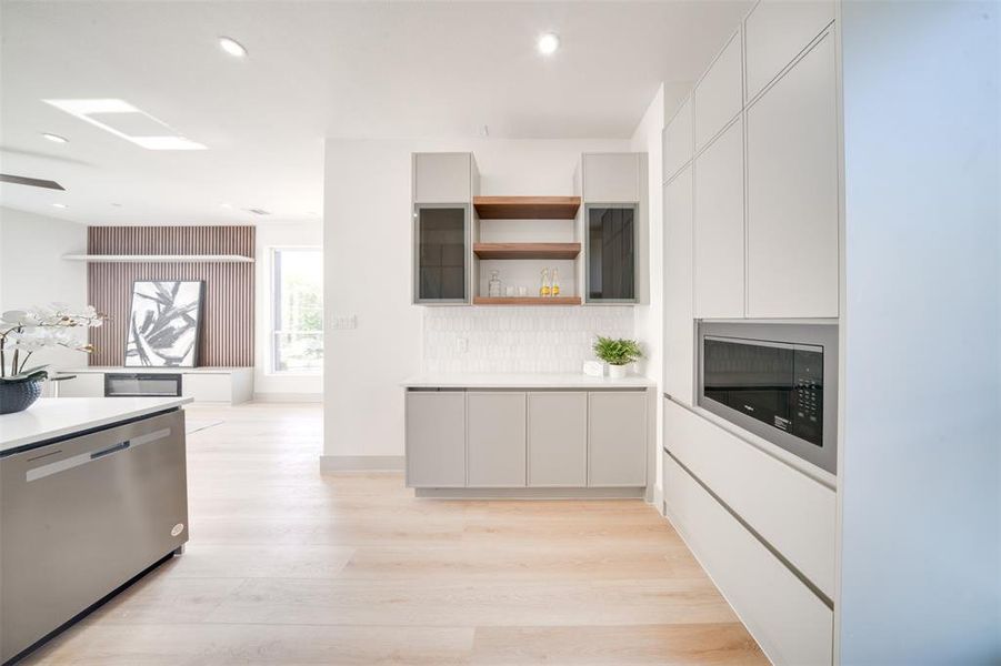 Kitchen featuring stainless steel dishwasher, light hardwood / wood-style flooring, white cabinetry, and tasteful backsplash