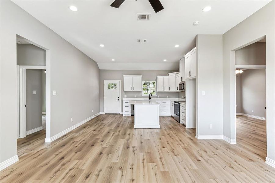 Kitchen with light wood-type flooring, appliances with stainless steel finishes, white cabinetry, an island with sink, and ceiling fan