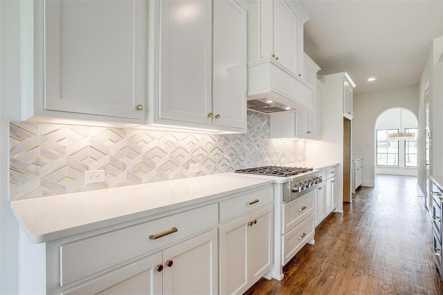Kitchen featuring custom range hood, tasteful backsplash, stainless steel gas stovetop, white cabinetry, and dark wood-type flooring