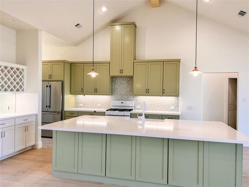 Kitchen with high vaulted ceiling, hanging light fixtures, range with gas stovetop, and a kitchen island with sink