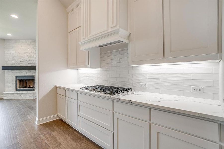 Kitchen with light stone counters, white cabinets, stainless steel gas cooktop, light hardwood / wood-style flooring, and a fireplace