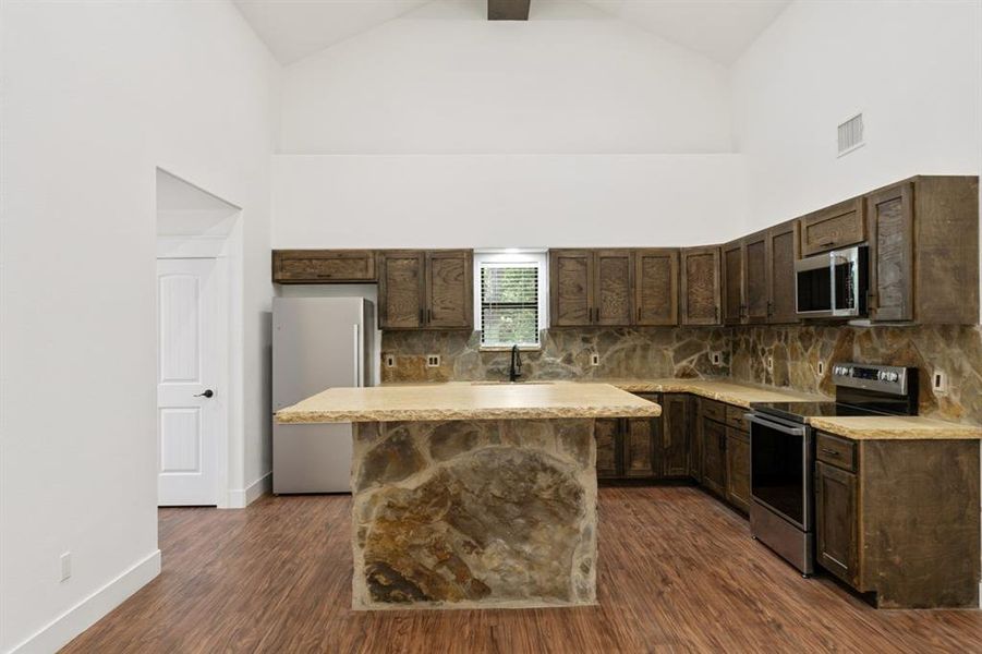 Kitchen with a center island, dark hardwood / wood-style flooring, stainless steel appliances, and high vaulted ceiling