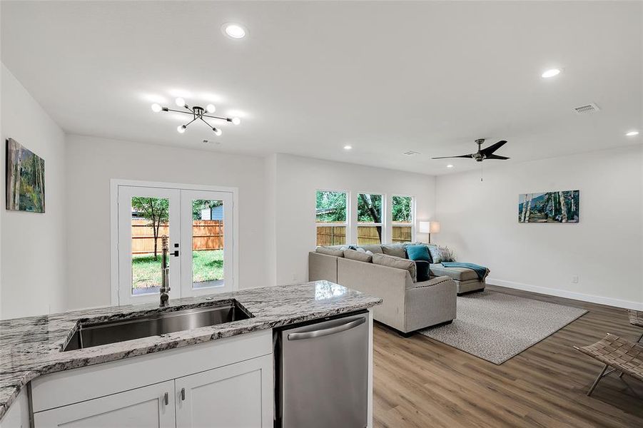 Kitchen with light wood-type flooring, ceiling fan with light granite counters, dishwasher, and white cabinets