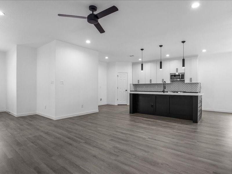 Kitchen with white cabinets, ceiling fan, hanging light fixtures, hardwood / wood-style flooring, and a center island with sink