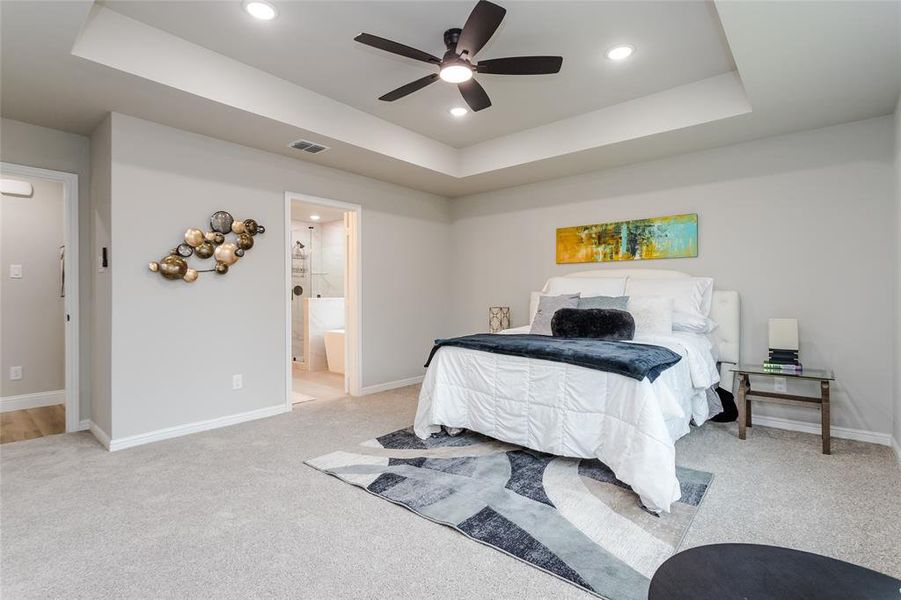 Carpeted bedroom with ceiling fan, ensuite bathroom, and a raised ceiling