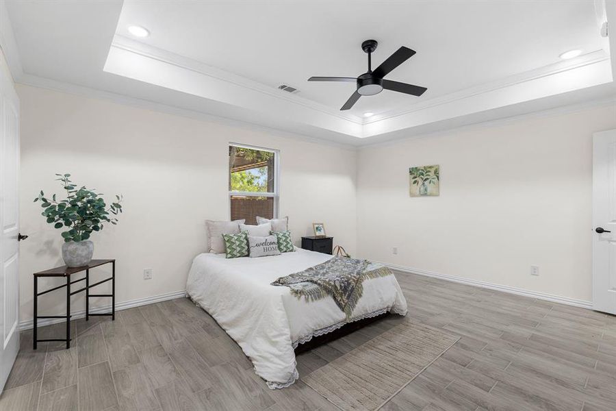 Bedroom featuring ceiling fan, ornamental molding, light wood-type flooring, and a tray ceiling