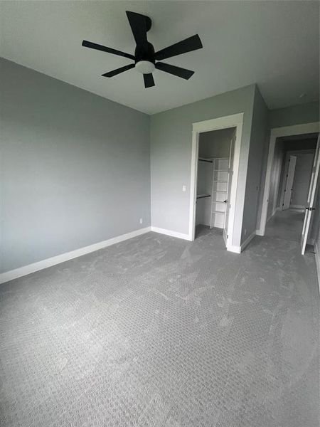 Unfurnished bedroom with dark colored carpet, a closet, a walk in closet, and ceiling fan