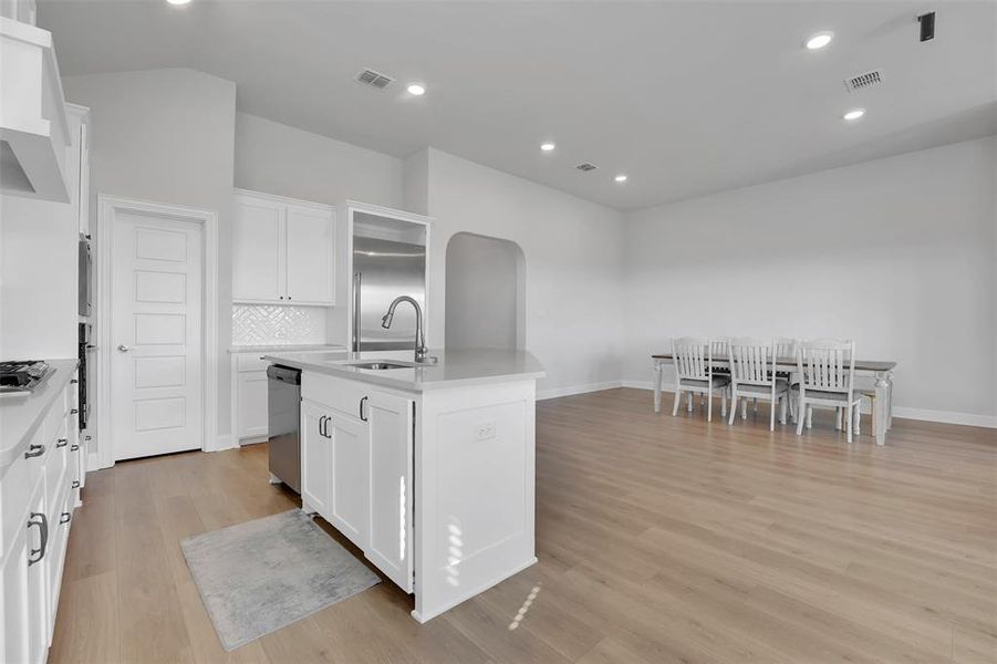 Kitchen featuring light hardwood / wood-style floors, white cabinetry, stainless steel appliances, a center island with sink, and sink