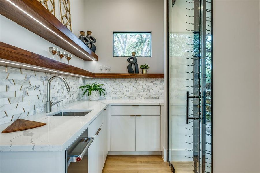 Bar with light stone counters, decorative backsplash, light hardwood / wood-style floors, and sink