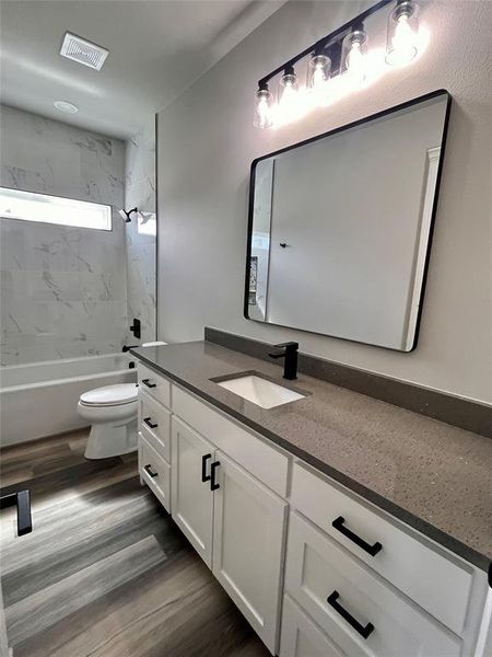 Full bathroom featuring wood-type flooring, tiled shower / bath, vanity, and toilet