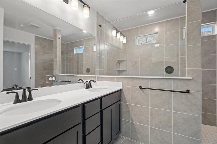 Bathroom with a tile shower, tile patterned flooring, tile walls, and vanity