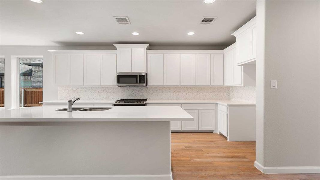 Kitchen with appliances with stainless steel finishes, light wood-type flooring, white cabinets, and backsplash