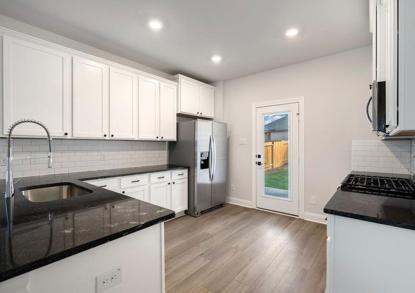 Chef-ready kitchen with black countertops, white cabinetry, and wood-style flooring.