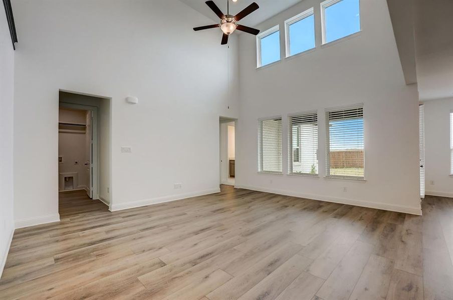 Unfurnished living room featuring a wealth of natural light, light hardwood / wood-style floors, a high ceiling, and ceiling fan