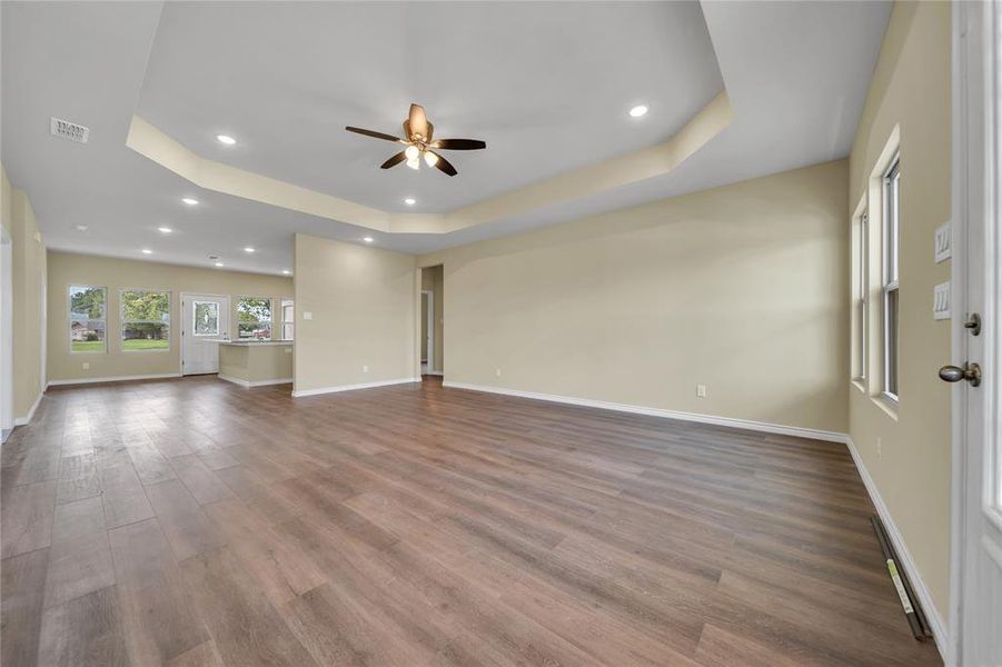 Unfurnished living room featuring hardwood / wood-style flooring, ceiling fan, and a tray ceiling