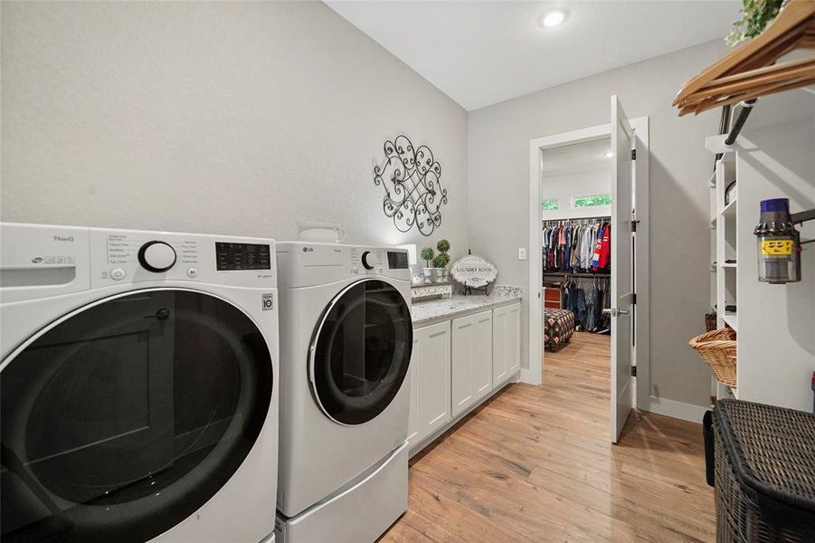 This custom utility room offers built-in storage solutions with a granite topped bank of storage cabinets, open shelving, and hanging bars for clothes. Notice the convenient access to the primary suite's walk-in closet pictured here.