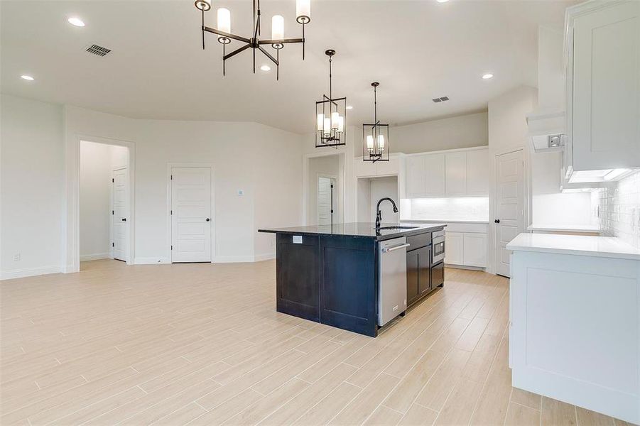 Kitchen featuring a kitchen island with sink, pendant lighting, white cabinetry, light hardwood / wood-style flooring, and dishwasher