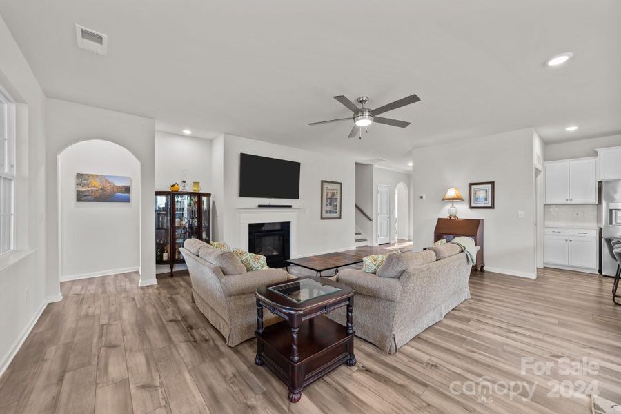 Huge open great room space with architectural details such as arched doorways, inset cove with recessed lighting, gas fireplace with mantel and tv hookup accessibility.