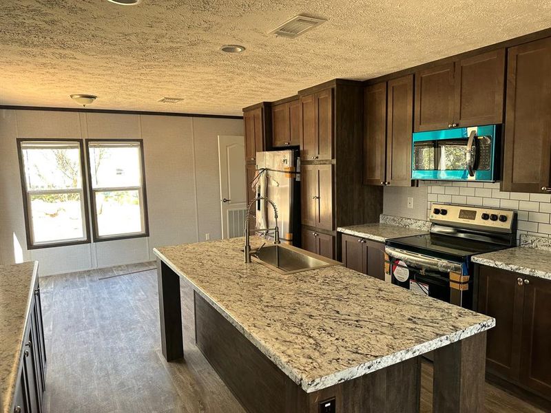 Kitchen with a kitchen island with sink, backsplash, pendant lighting, appliances with stainless steel finishes, and light stone counters