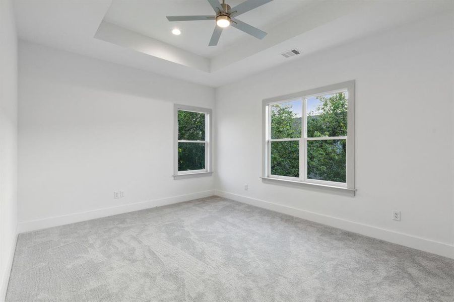 Empty room with a raised ceiling, light carpet, and ceiling fan