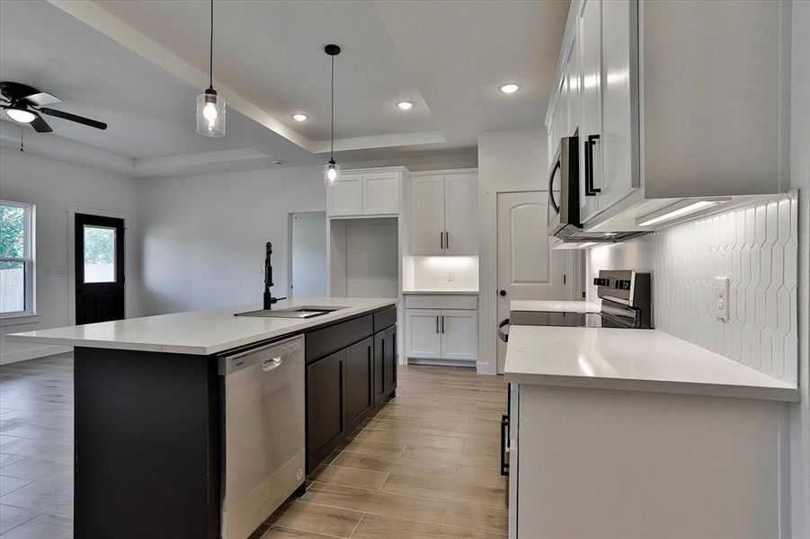 Kitchen with a center island with sink, hanging light fixtures, stainless steel appliances, sink, and white cabinets