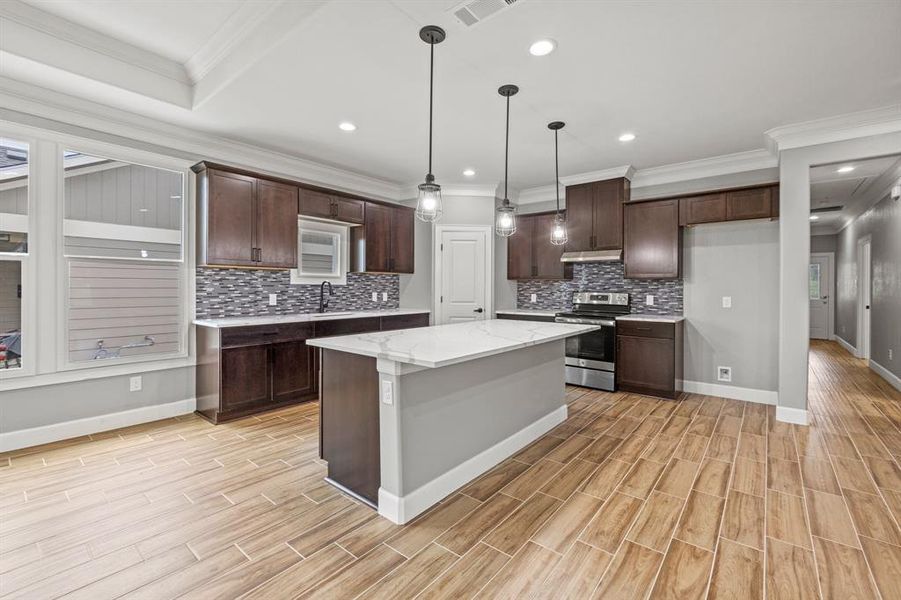 Kitchen with a center island, light stone countertops, stainless steel range with electric stovetop, decorative light fixtures, and tasteful backsplash