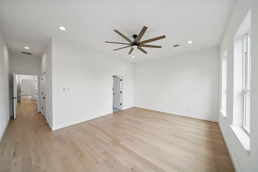 This is a spacious, modern room with high ceilings, light hardwood flooring, contemporary ceiling fan, recessed lighting, and large windows providing ample natural light. The room offers a clean, blank canvas ideal for personalization.
