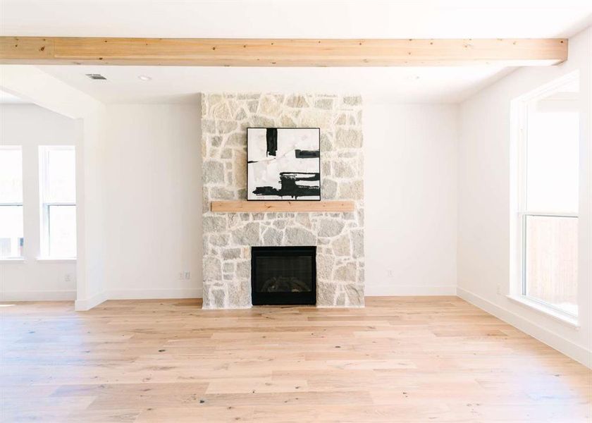 Unfurnished living room with light hardwood / wood-style floors, a stone fireplace, and beam ceiling