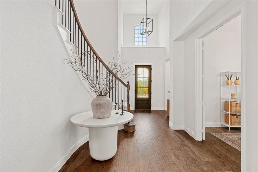 Foyer entrance with dark wood-type flooring, a towering ceiling, and an inviting chandelier