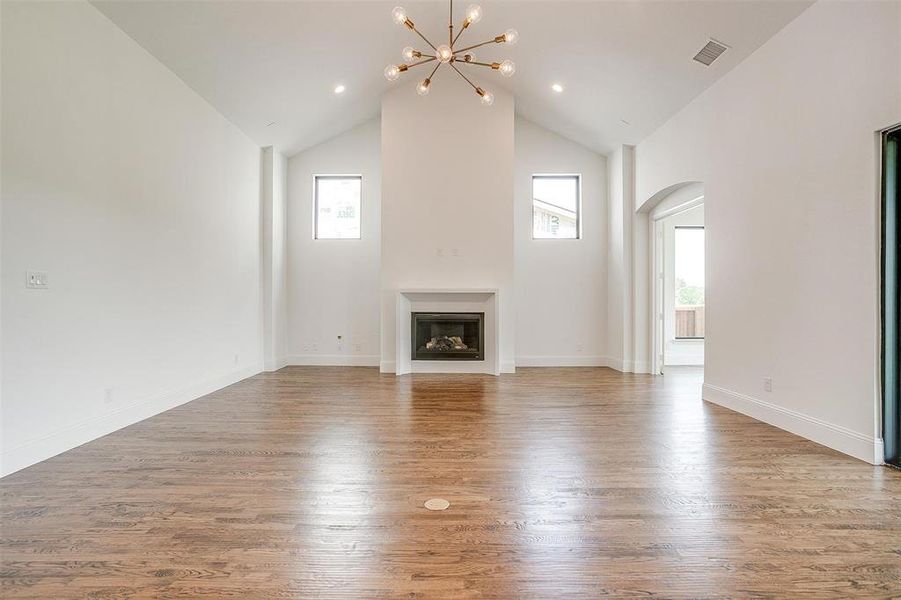 Unfurnished living room featuring high vaulted ceiling, an inviting chandelier, hardwood / wood-style floors, and a wealth of natural light