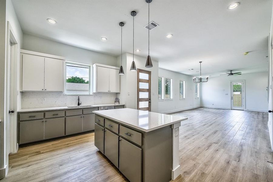 Kitchen with decorative light fixtures, a center island, gray cabinets, white cabinetry, and light wood-type flooring