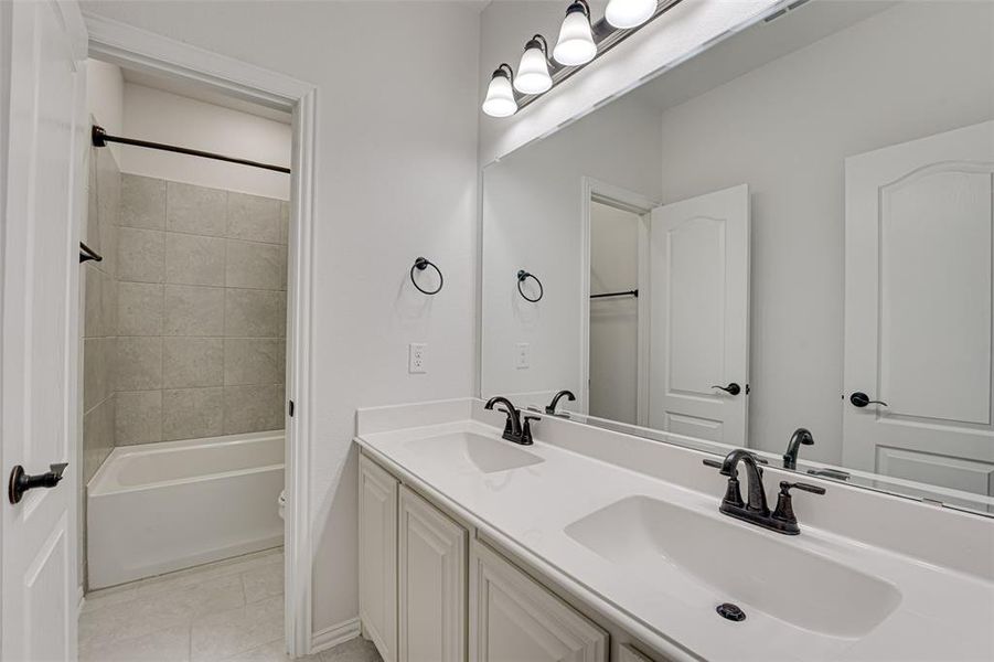 Full bathroom with dual vanity, tiled shower / bath, tile patterned flooring, and toilet