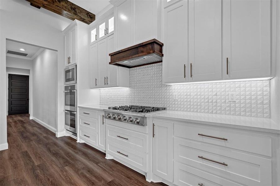 Kitchen featuring stainless steel appliances, tasteful backsplash, white cabinetry, dark wood-type flooring, and beamed ceiling