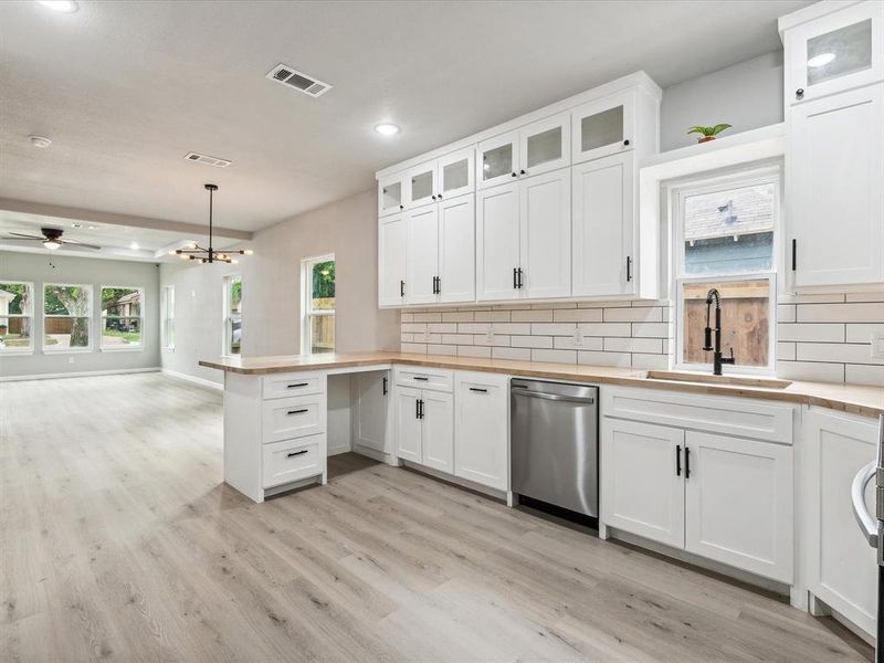 Kitchen featuring hanging light fixtures, dishwasher, light hardwood / wood-style flooring, ceiling fan with notable chandelier, and sink