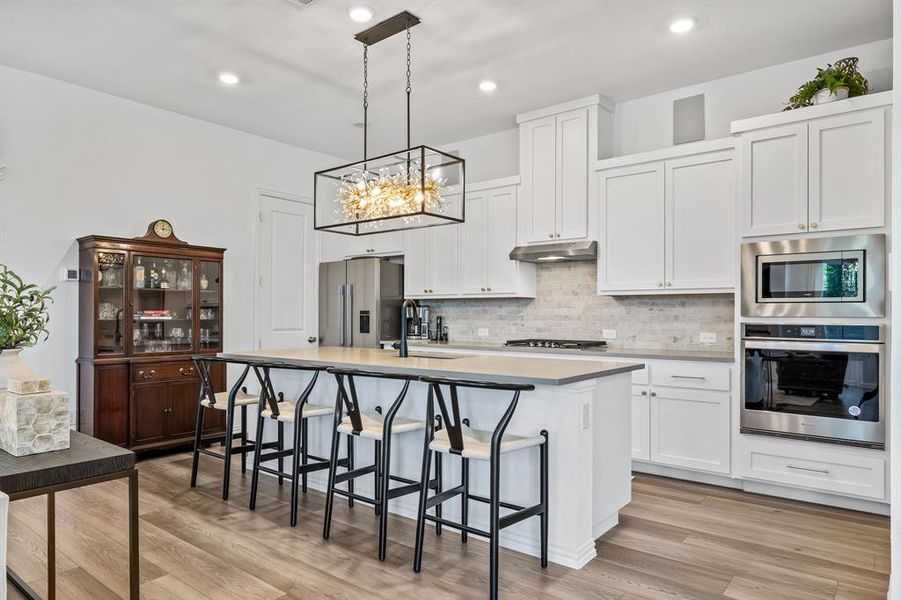 Kitchen featuring stainless steel appliances, white cabinets, a center island with sink, and light hardwood / wood-style flooring