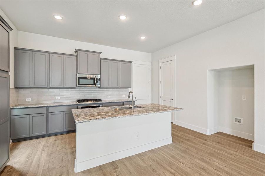 Kitchen featuring stainless steel appliances, light hardwood / wood-style floors, gray cabinets, and light stone countertops