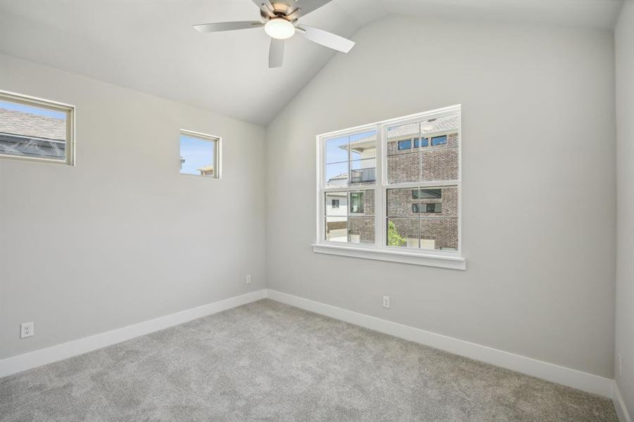 Carpeted empty room featuring ceiling fan and vaulted ceiling