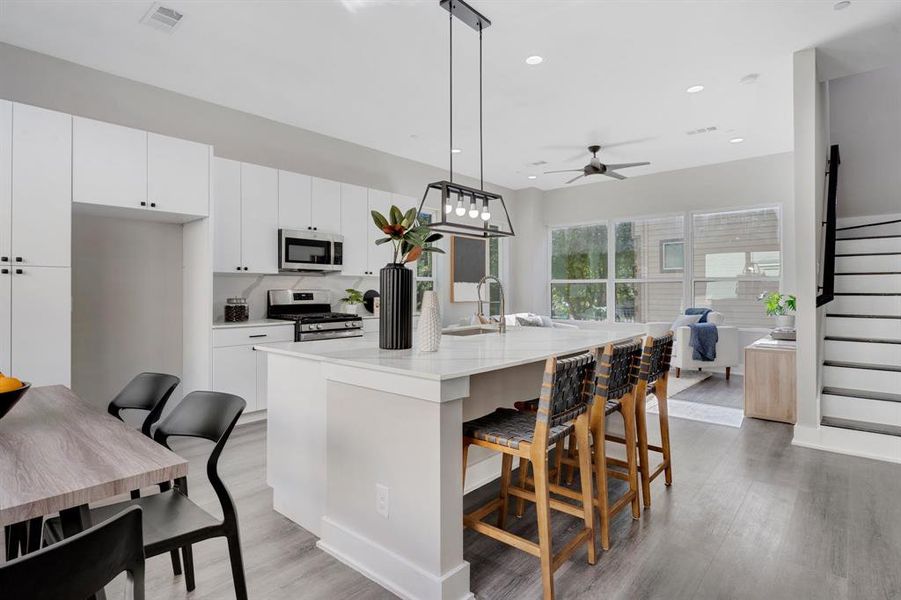 Kitchen featuring decorative light fixtures, ceiling fan, a center island with sink, light hardwood / wood-style floors, and appliances with stainless steel finishes