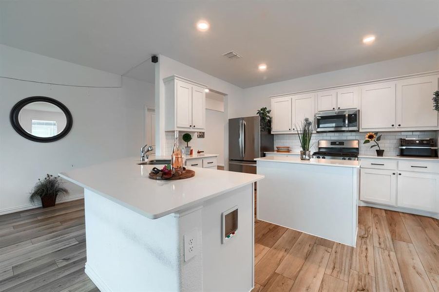 Kitchen with stainless steel appliances, light hardwood / wood-style floors, white cabinetry, backsplash, and a center island