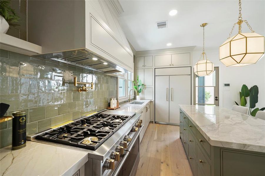 Elegant chef's kitchen featuring high-end GE Monogram appliances, dual oven range, soft closing drawers and cabinets, under mount lighting, stylish pendant lighting with a green tile backsplash.