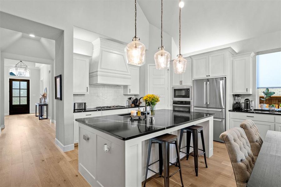 Kitchen featuring light hardwood / wood-style floors, tasteful backsplash, custom exhaust hood, a center island, and appliances with stainless steel finishes